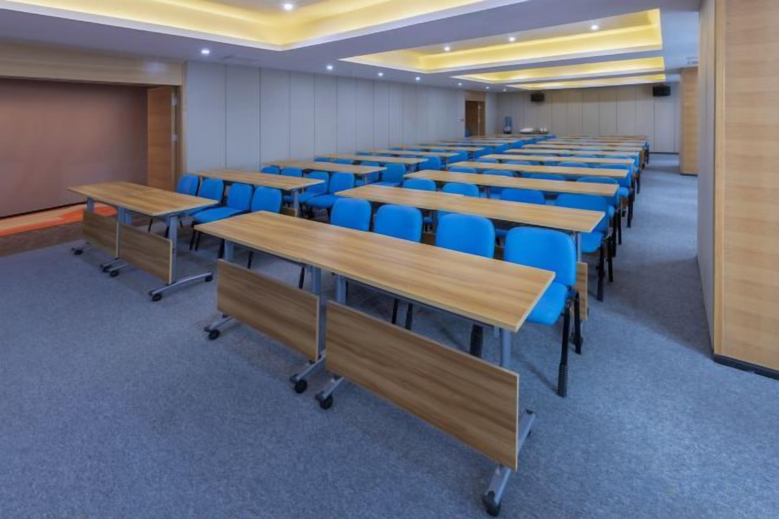 A conference room with rows of tables and chairs, carpeted floor, and a neutral color scheme.