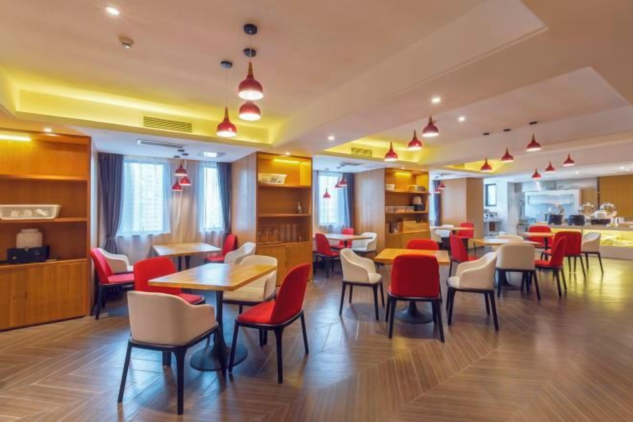 Interior moderno de restaurante com várias mesas e cadeiras, luminárias pendentes vermelhas e área de cozinha ao fundo.