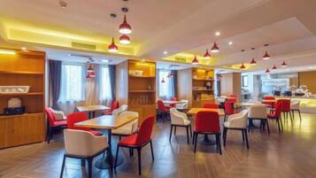 Interior moderno de restaurante con varias mesas y sillas, iluminación colgante roja y una zona de cocina al fondo.