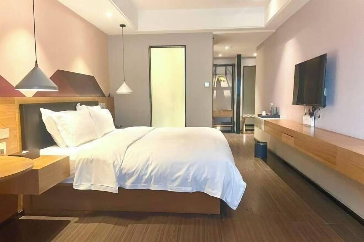A modern hotel room with a large bed, bedside tables, a TV, and a bathroom visible through an open door.