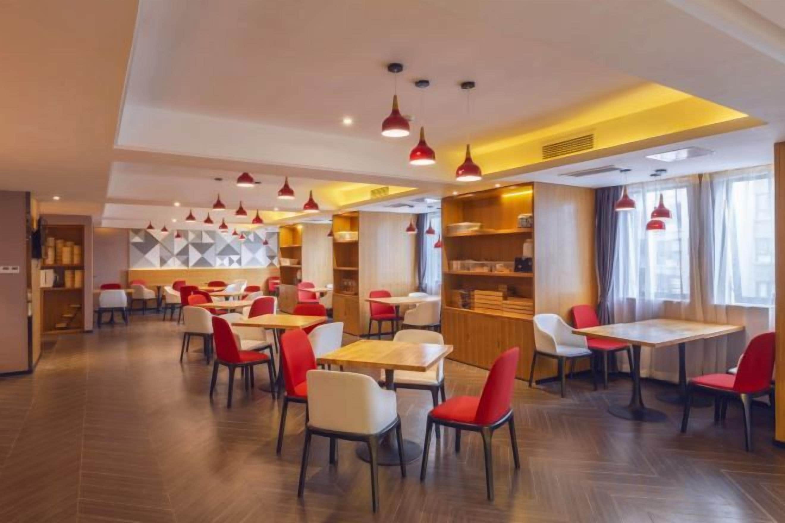 Un restaurante moderno con varias mesas y sillas, una zona de cocina y vistas a la ciudad a través de amplios ventanales.