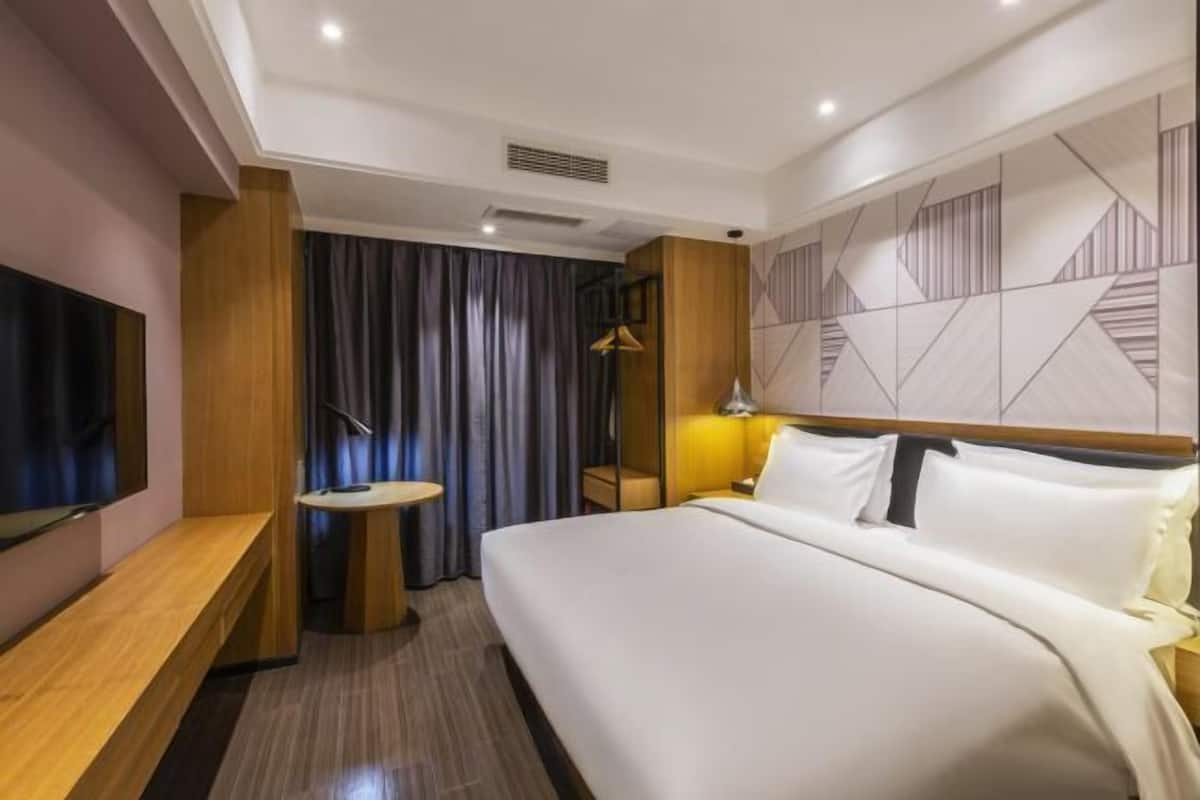 A hotel room with a bed, a TV, a desk, and a mirror.
