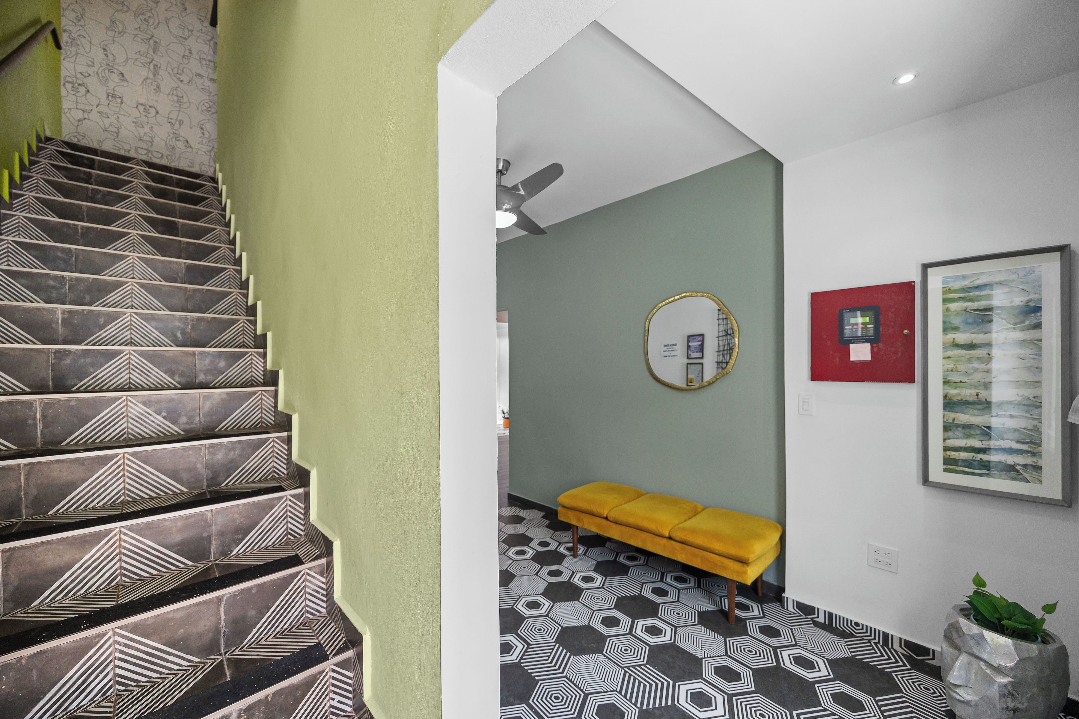 Eine Treppe mit geometrischen Mustern, eine gelbe Bank, ein Deckenventilator und ein gerahmtes Kunstwerk an der Wand.