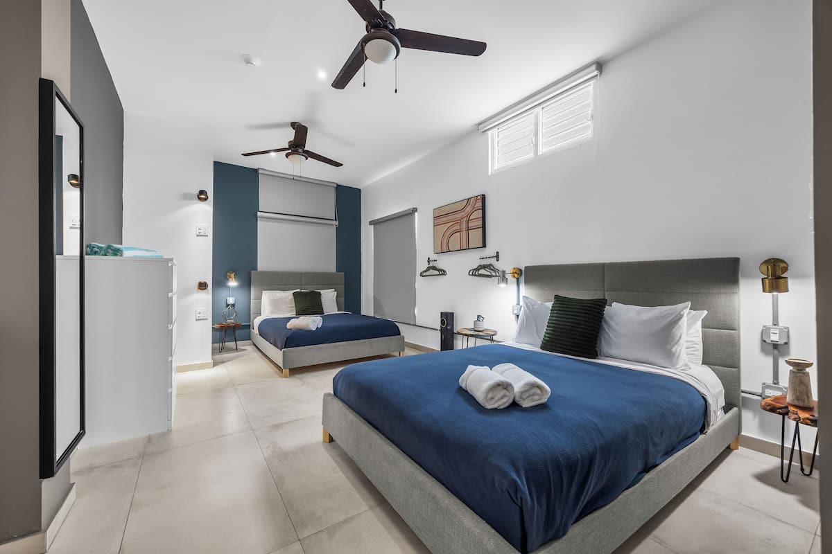 A modern bedroom with two beds, ceiling fans, a large mirror, and a bedside table with a lamp.