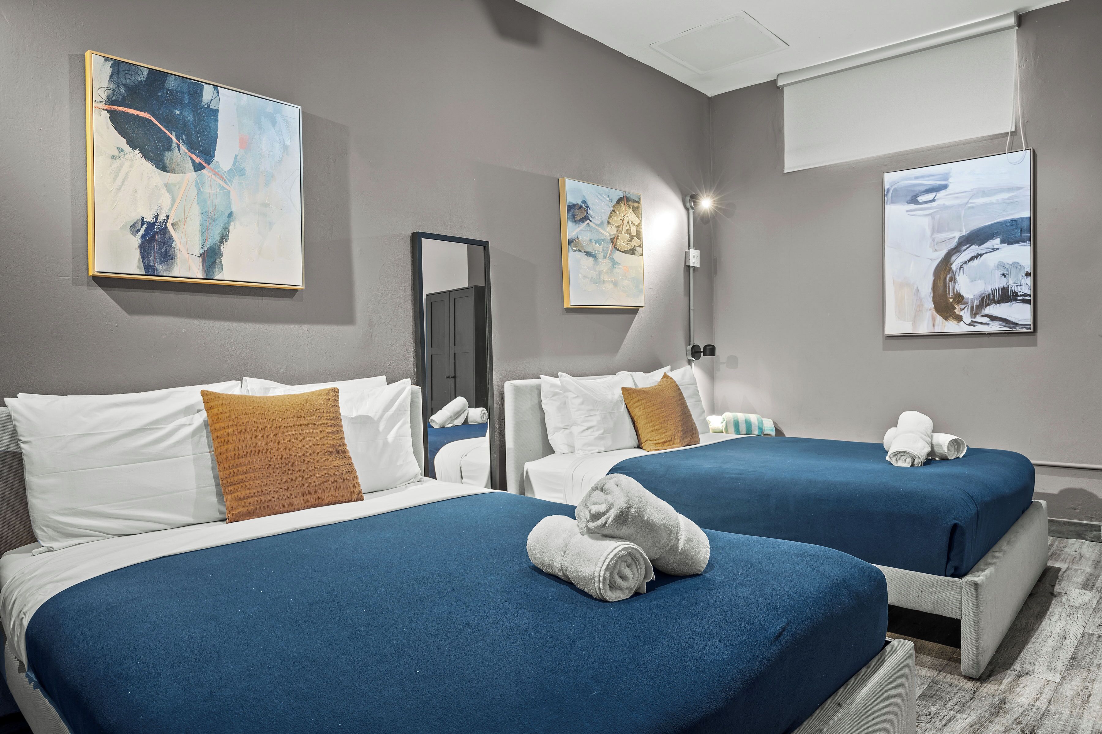 Ein Hotelzimmer mit zwei Betten, beide mit blauer Bettwäsche und weißen Kissen. Auf den Betten liegen Handtücher und die Wände sind mit Bildern dekoriert.