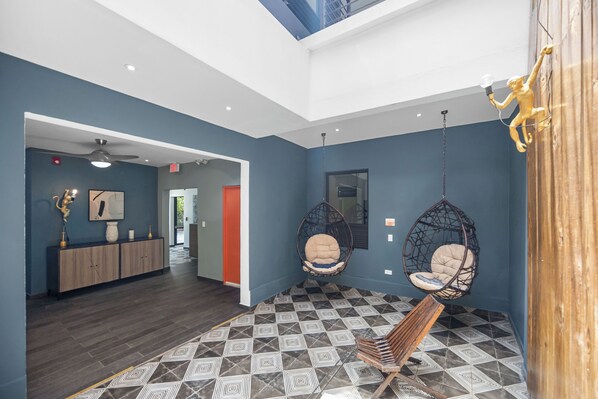 A modern interior with a geometric patterned floor, a reception desk, and two hanging chairs. - La Buena Vida Inn (San Juan)