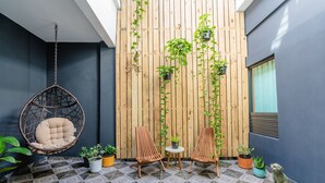 A modern outdoor seating area with a hanging chair, two wooden chairs, and potted plants against a wooden backdrop. - La Buena Vida Inn (San Juan)