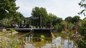 Un jardín con un estanque, una terraza de madera y un sofá exterior negro.