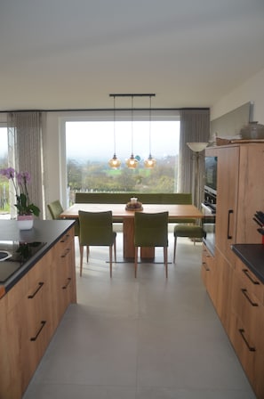 A modern kitchen with wooden cabinets, a dining table with chairs, and a large window offering a view of the outdoors. - Exclusive vacation home in the middle of the vineyards with fantastic views (Ilsfeld)