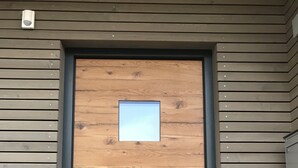 Una puerta de madera con un pequeño ventanal, integrada en un edificio moderno con revestimiento horizontal.