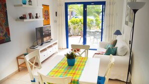 A living room with a TV, a dining table with chairs, a sofa, and a view of the outside. - House Maresía Las Moreras Duplex with Sea View 1 minute from the seafront promenade  (Playa Blanca)