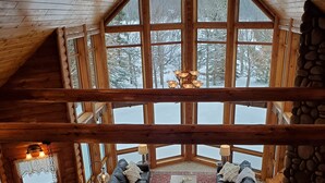 A cozy cabin interior with a stone fireplace, a stone-tiled floor, a wooden ceiling, and a large window overlooking a snowy landscape. - Lakefront secluded mult-family retreat with game room and two cabins.  (Townsend)