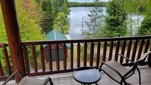 A wooden deck with two chairs and a table overlooking a lake, surrounded by trees. - Lakefront secluded mult-family retreat with game room and two cabins.  (Townsend)