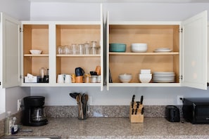 Uma cozinha com armários abertos exibindo pratos, copos e utensílios.