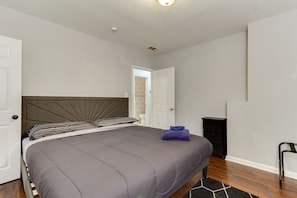 Quarto com uma cama grande, mesa de cabeceira, cadeira e porta para um banheiro.