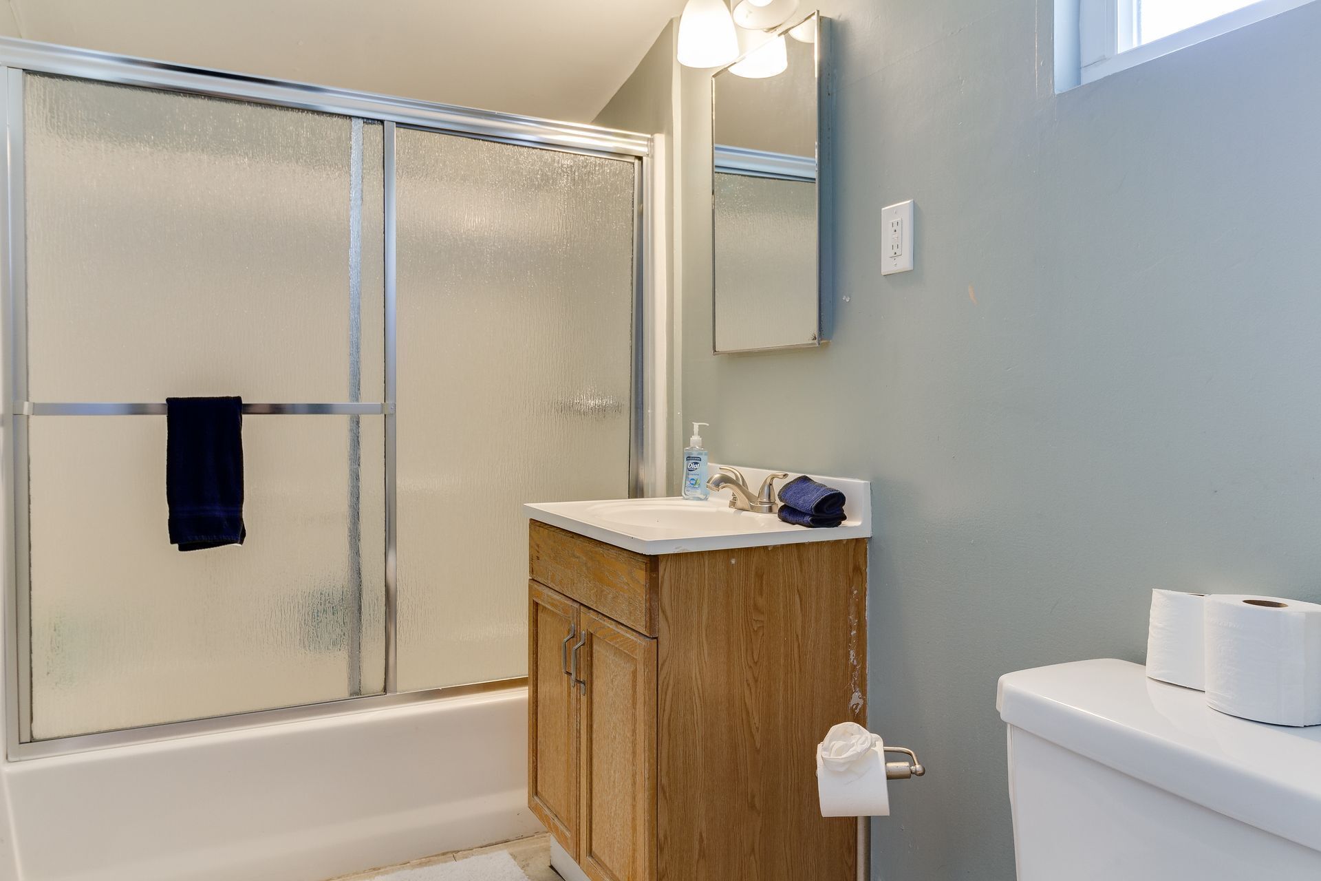A bathroom with a glass shower door, a wooden vanity, a white sink, and a toilet.