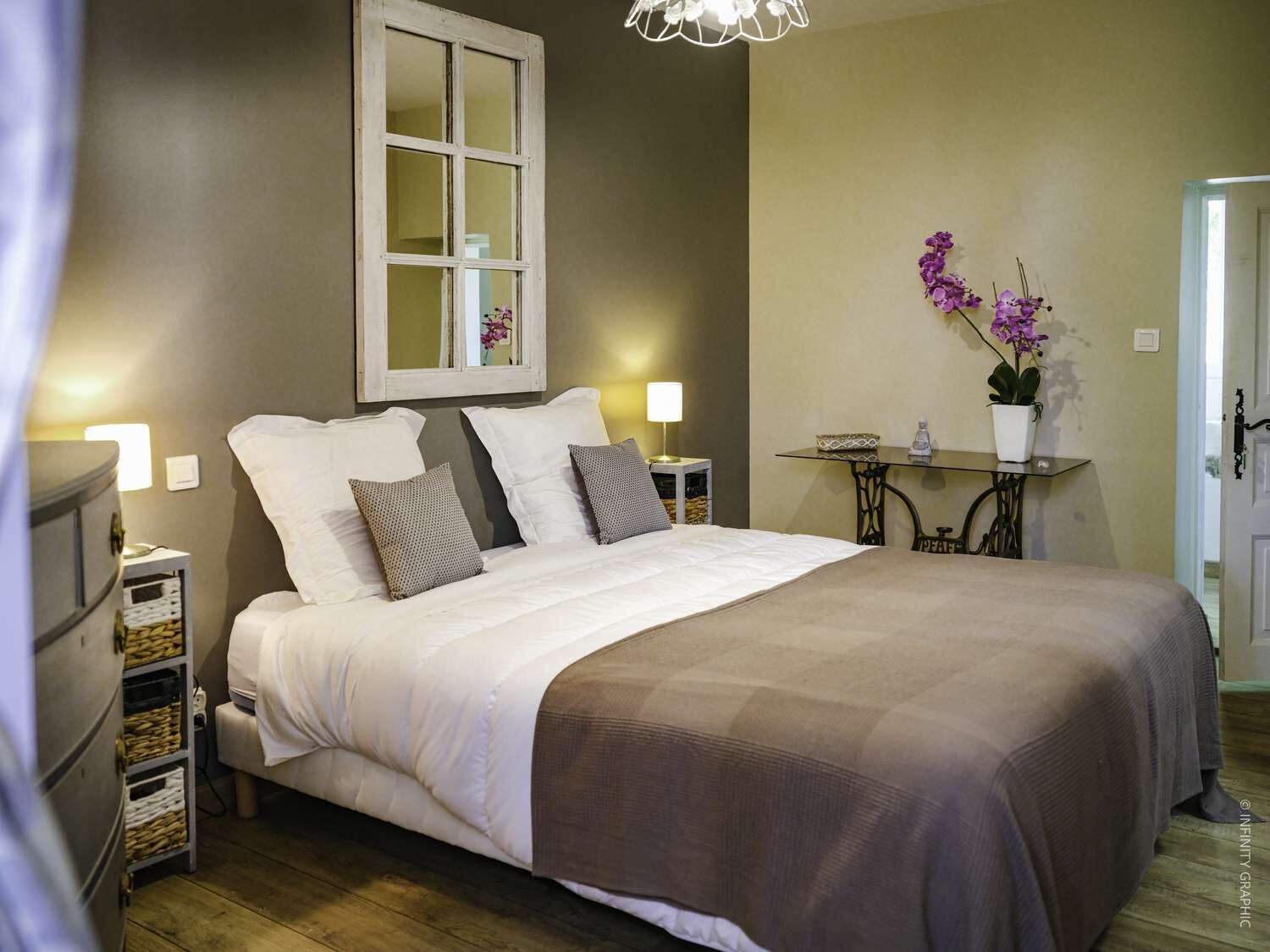 Une chambre à coucher avec un grand lit, des tables de chevet, un miroir et une petite table sur laquelle est posée une plante.