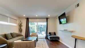 Una sala de estar moderna con un sofá, un reposapiés y un televisor de pantalla plana montado en la pared.