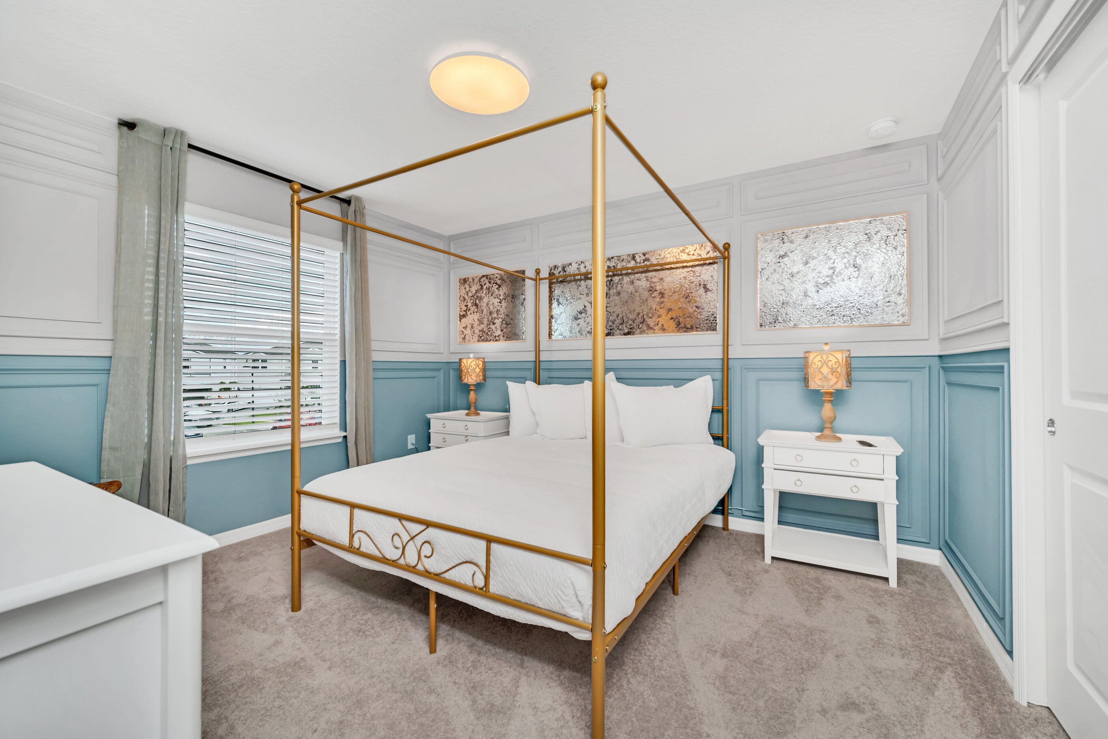 A four-poster bed with a gold frame, a white bedside table with a lamp, and a blue accent wall.