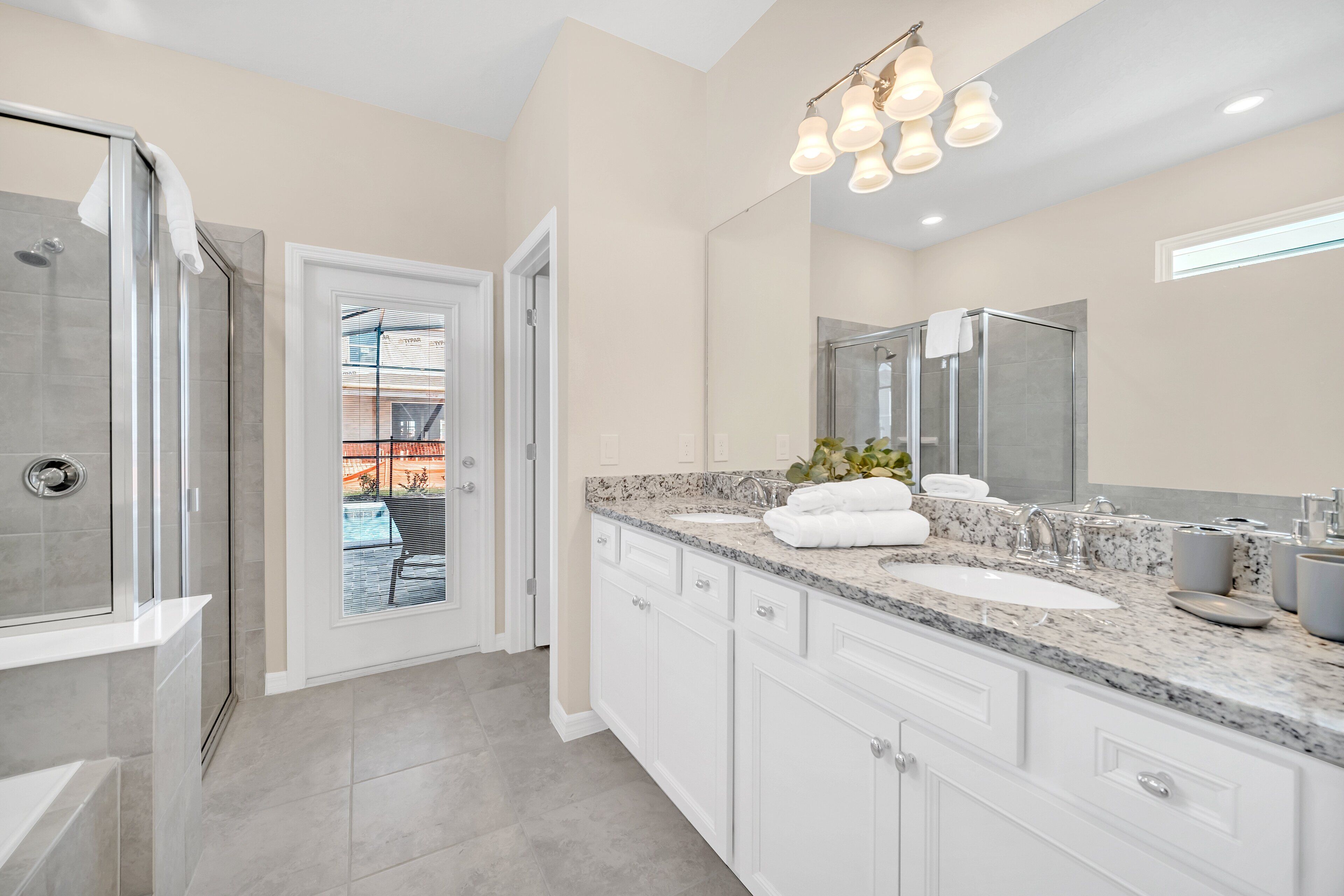 A modern bathroom with a walk-in shower, a large vanity with a granite countertop, and a large mirror.