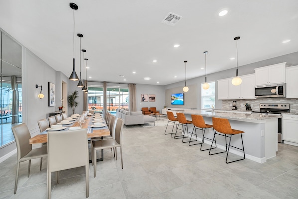 A modern kitchen with a central island, white cabinetry, and a dining area with a long table and chairs.