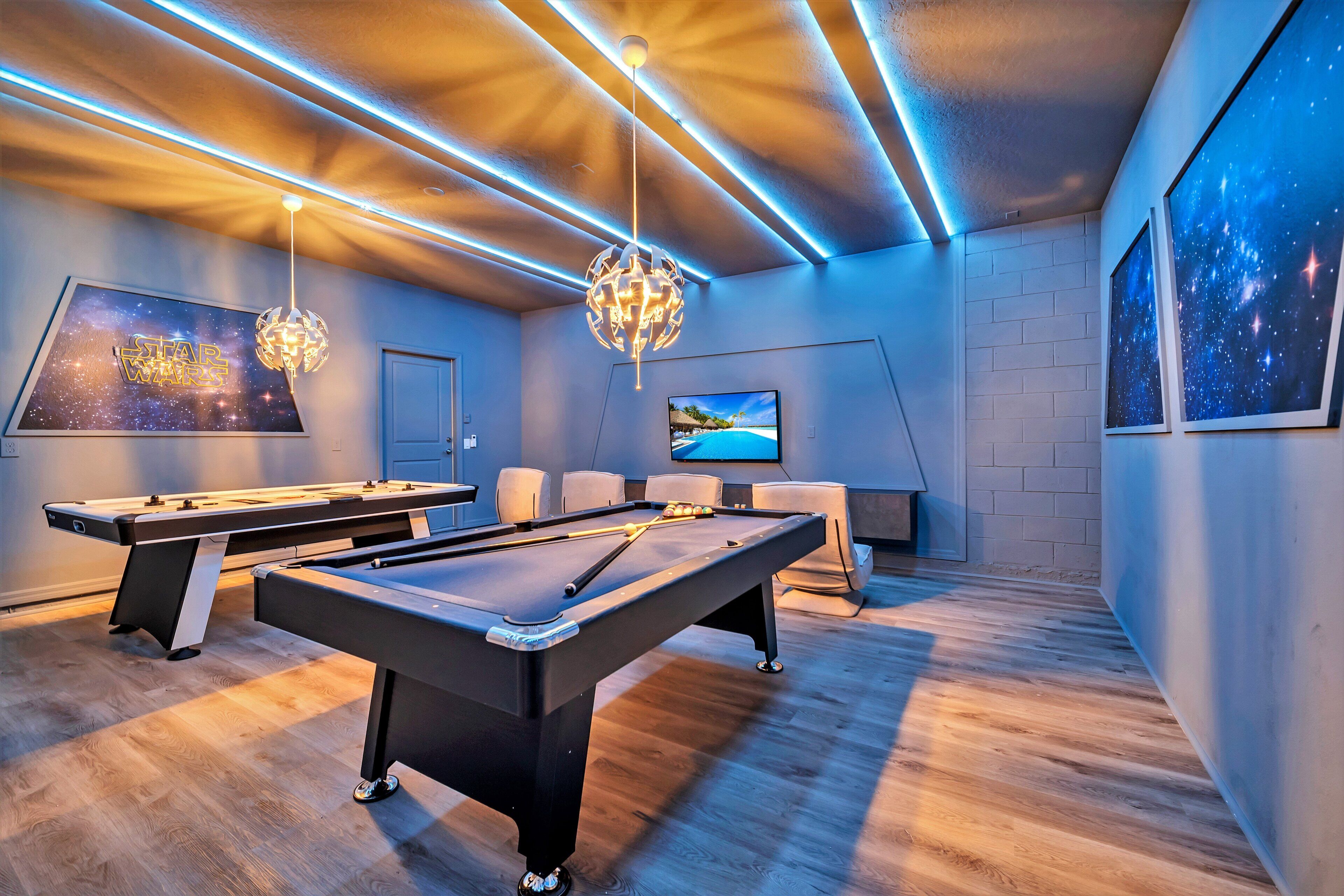 A pool table with a billiards setup, a television screen, and a Star Wars-themed wall art.