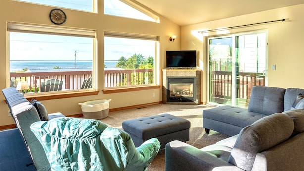 A living room with a fireplace, large windows, and a view of the ocean. - Dune Breeze - Wifi and Hot tub (Pacific Beach)