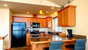 A kitchen with wooden cabinets, a black refrigerator, a microwave, an oven, a sink, and a bar area with two blue chairs. - Dune Breeze - Wifi and Hot tub (Pacific Beach)