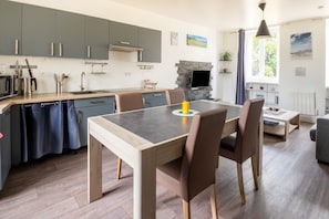 A modern kitchen with grey cabinets, a central island, and a dining area with brown chairs.