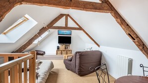 A cozy attic bedroom with a sloped ceiling, wooden beams, a bunk bed, a sofa, a TV, and a radiator.