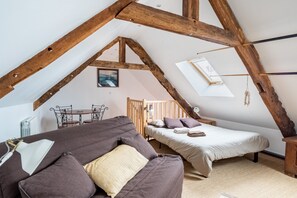 A cozy attic bedroom with exposed wooden beams, a loft bed, a sofa, and a small dining table.