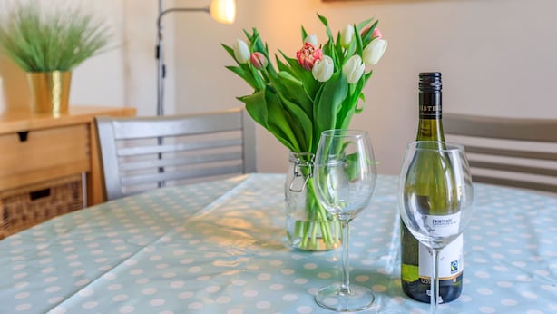 A table with a polka dot tablecloth, a vase with tulips, two wine glasses, and a wine bottle. - Sea Spray (Watchet)