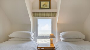 A bedroom with two beds, a window with a view, a bedside lamp, and a framed picture on the wall. - Sea Spray (Watchet)