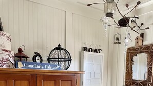 A wooden cabinet with multiple drawers, a white wall with vertical paneling, a white chair with a striped cushion, a hanging birdcage, and a wall-mounted mirror with a rustic frame.