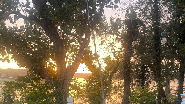 A hot tub with steps and a table on a wooden deck, surrounded by trees and a view of the sunset.