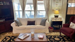 A living room with a white sofa, a coffee table with books and a glass jar, a lamp, and a fish identification chart on the wall.