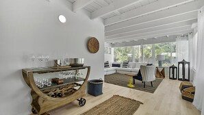 Amplia sala de estar con un carrito de madera, un sofá y un ventanal con persianas.