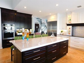 A modern kitchen with dark cabinetry, a central island, and stainless steel appliances. - 5 Bedroom Luxe Villa on Deep Water Intracoastal (Deerfield Beach)