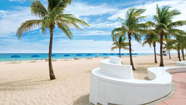 A beach with white curvilinear structures, palm trees, and blue umbrellas. - Walk to Fort Lauderdale Beach - Perfect Beach Escape (Fort Lauderdale)