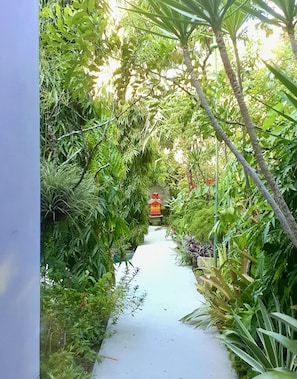 Stroll through lush gardens along a well-maintained pathway to a charming structure with a distinctive red roof.