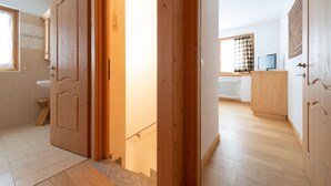 Een kamer met houten deuren, een badkamer met toilet en wastafel, een houten vloer en een raam met uitzicht.