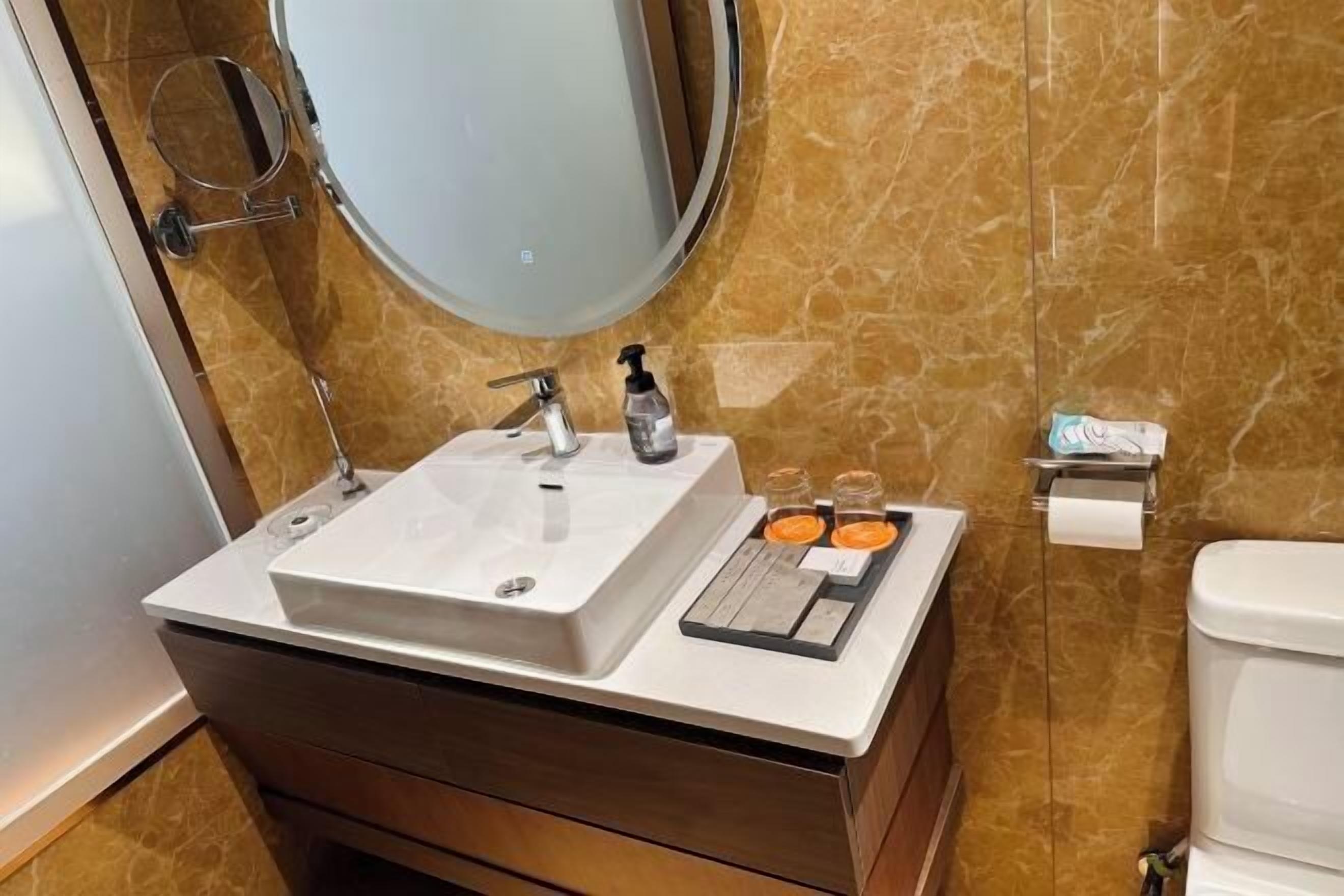 A bathroom with a white sink, a mirror, a toilet, and a small shelf with toiletries.