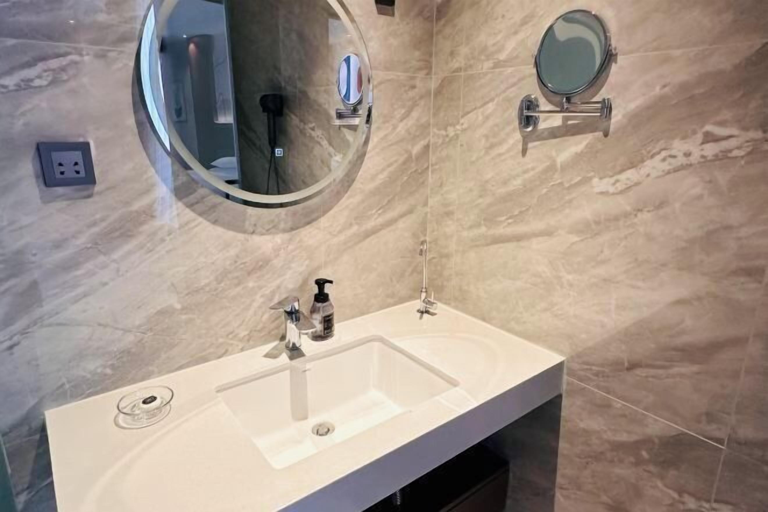 A bathroom with a white sink, two wall-mounted mirrors, and a marble-tiled wall.