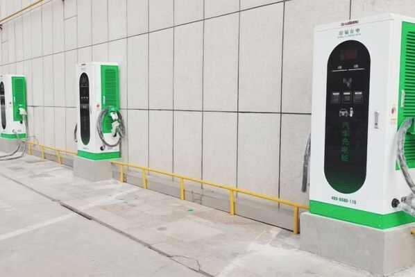 Filera d'estacions de càrrega per a vehicles elèctrics amb una combinació de colors verd i blanc, connectades a una font d'energia.