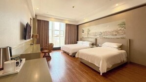Een hotelkamer met twee bedden, een bureau, een stoel, een flatscreen televisie en een groot raam met gordijnen.