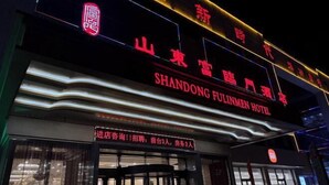 Het uiterlijk van het Shandong Fulinmen Hotel met verlichte borden en een draaideur.