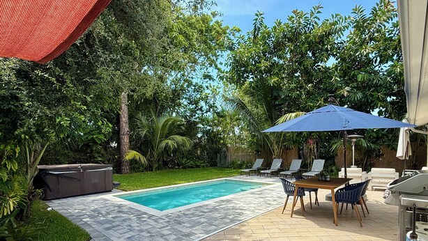 A swimming pool with a tiled deck, surrounded by lush greenery and a barbecue area with outdoor furniture. - AVAILABLE NOW!! FERN COTTAGE! FREE beach parking! Weekly/Monthly/Yearly Rentals! (Naples)