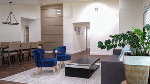 Ein modernes Wohnzimmer mit Essbereich, einem blauen Sessel, einem Couchtisch und einer großen Kühlpflanze.