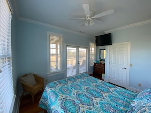 A bedroom with a bed, a ceiling fan, a TV mounted on the wall, and a door leading to another room. - "Cape View" Relaxing home with private dock on the ICW with Lighthouse Views! (McClellanville)