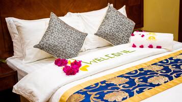 A neatly made bed with a 'WELCOME' sign, pillows, and a decorative blue and gold bedspread.